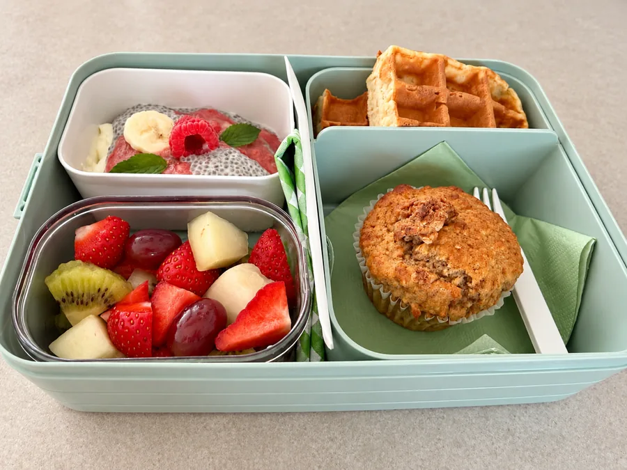 Die mintgrüne Mehrwegbox von der Seite, gefüllt mit Obst, Chia-Skyr, Waffel und Muffin